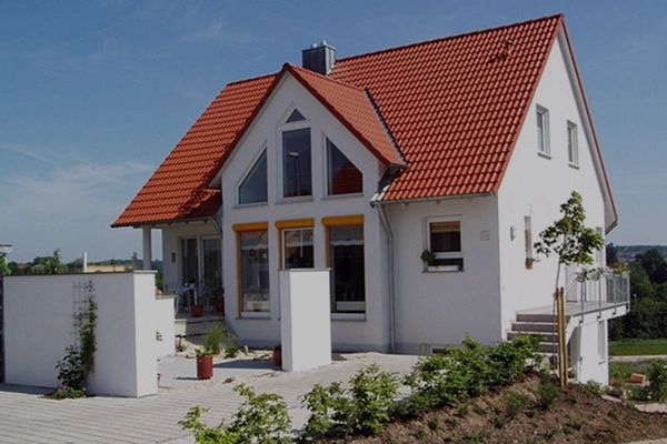 Einfamilienhaus mit rotem Dach und weißer Fassade als Beispiel für eine Lösung zur Wasseraufbereitung im privaten Bereich.